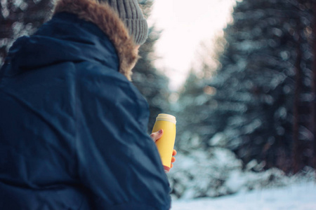 冬天森林里的一个旅行者猎林者坐在倒下的树上，手里拿着热水瓶