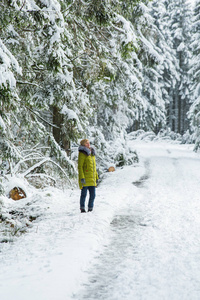 一个年轻的女人正在白雪覆盖的树林间穿过冬林