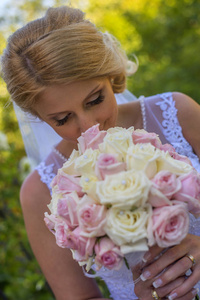 新娘穿着婚纱闻着她的花束，身上有粉红色和黄色的玫瑰。 在澳大利亚惊人的沙滩上参加婚礼。