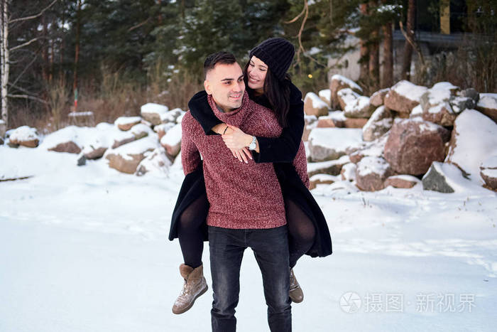 快乐的年轻男友在冬天在森林公园背着他的女朋友.