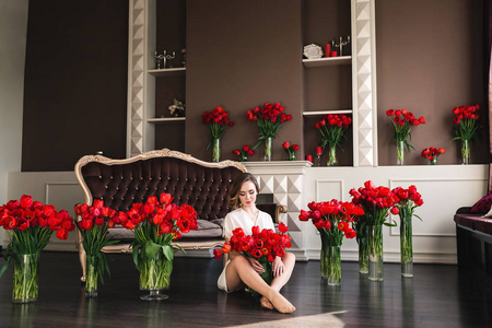一个穿着小房间的美丽年轻女孩坐在客厅的地板上, 夹在大花束之间。概念3月8日