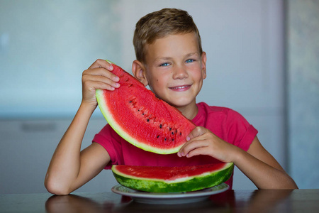 可爱的孩子享受夏天多汁的浆果，水果，西瓜，英俊的蓝眼睛，男孩穿着红色的t恤，在家里的工作室厨房里分离出一片西瓜