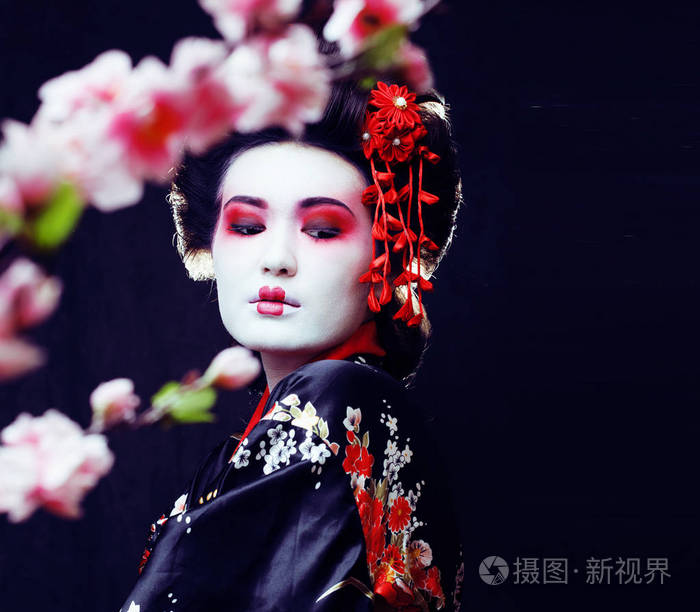 年轻漂亮真正的艺伎在和服与樱花和装饰