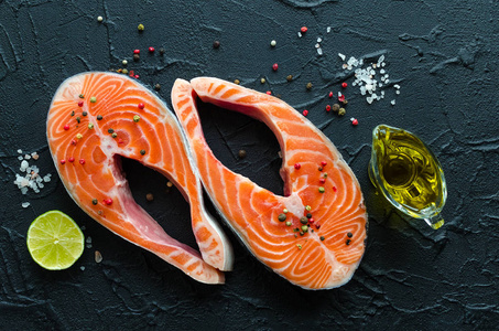 两个新鲜的生鲑鱼牛排与胡椒玉米，盐，柠檬和橄榄油在黑色背景。 健康食品饮食理念。 准备用香料煮鱼。 上面的风景。