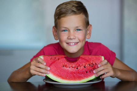 可爱的孩子享受夏天多汁的浆果，水果，西瓜，英俊的蓝眼睛，男孩穿着红色的t恤，在家里的工作室厨房里分离出一片西瓜