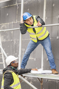 土木工程师用安全帽和黄夹克检查施工现场脚手架的技术图纸和办公室蓝图