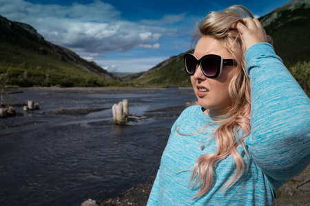 金发女性站在德纳利国家公园的野蛮河流附近，摆姿势看阿拉斯加的风景。