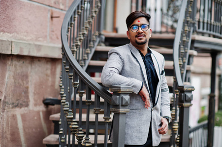时尚的印度男人额头上戴着Bindi，西装上戴着眼镜，摆在户外的铁楼梯上。