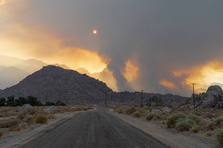 野火始于内华达山脉东部，靠近阿拉巴马山。 前景中的土路。 空气中有很多烟。 太阳是橙色的