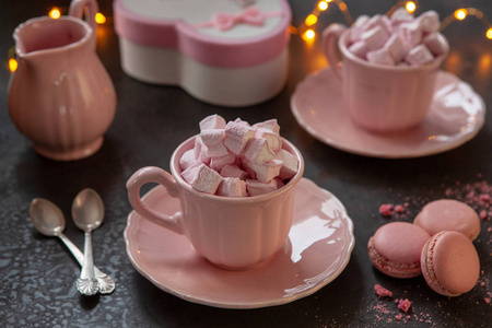 两个粉红色的杯子，粉红色的心形棉花糖，一个礼物在粉红色的盒子和粉红色的马卡龙。 两人的浪漫早餐。 关闭选择性聚焦。