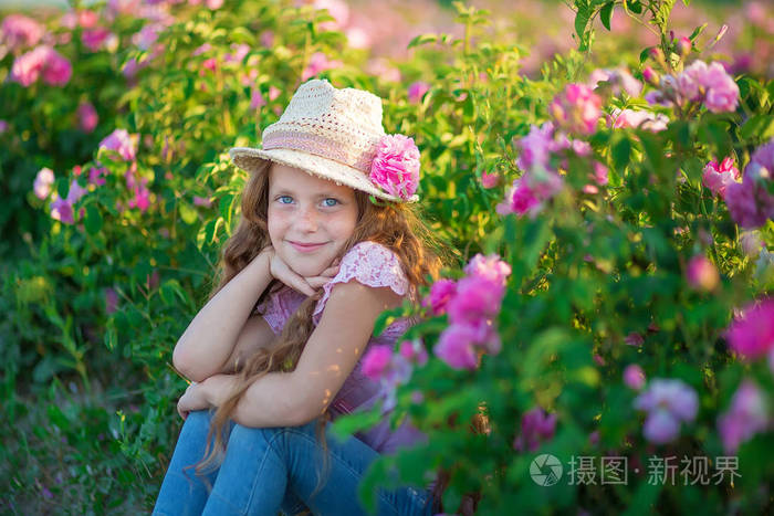 可爱的黑发孩子蓝眼睛女孩拿着花站在粉红色的玫瑰田.