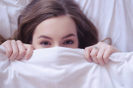 早上,睁开眼睛的十几岁的女孩用白色的毯子遮住了她的脸.