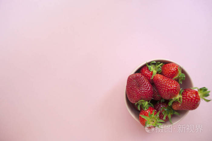 平躺着新鲜采摘的甜草莓在一个碗上涂上粉红色的背景。 健康的食物概念。