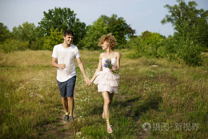 年轻可爱的夫妇享受大自然牵着手带着薰衣草在田野上散步春天日落时