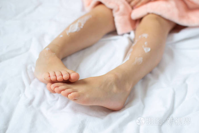 小女孩在腿上涂润肤霜护肤及美容概念