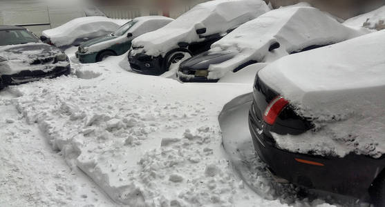 在十二月降雪期间，住宅区的停车场上覆盖着雪的汽车。