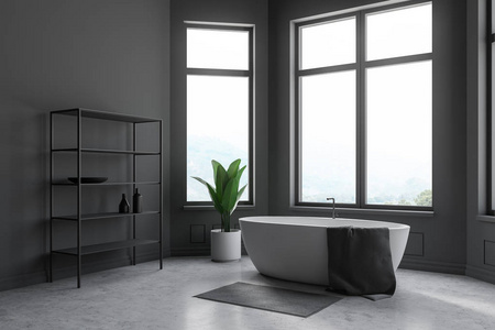 灰色浴室的角落,有混凝土地板,大窗户和白色浴缸,上面有毛巾,站在灰色