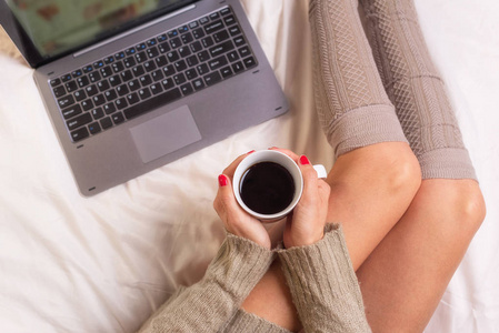 妇女在床上的软照片与笔记本电脑和一杯咖啡在手, 顶部的观点