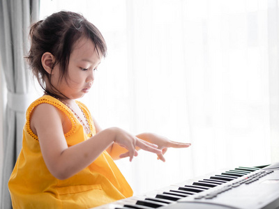 亚洲女孩在家的窗户附近弹键盘钢琴。