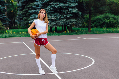 美丽的年轻女孩穿着白色 t恤, 短裤和运动鞋, 在篮球场上玩球