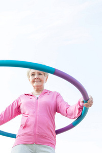 老年妇女用呼啦圈顶天锻炼的低角度视角