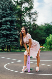 一个微笑的迷人的黑发女性拿着她的滑板在篮球场的肖像