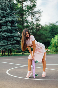 一个微笑的迷人的黑发女性拿着她的滑板在篮球场的肖像