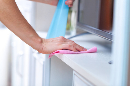 一个年轻的女人用抹布擦拭灰尘,并在房间里喷洒. 房屋清洁照片