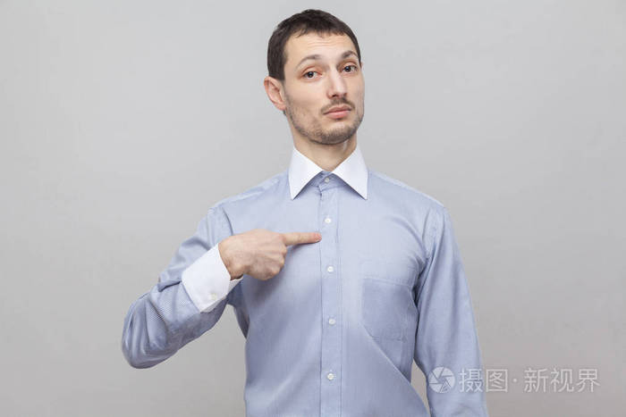 骄傲的商人的肖像,指着自己,看着灰色背景上的照相机