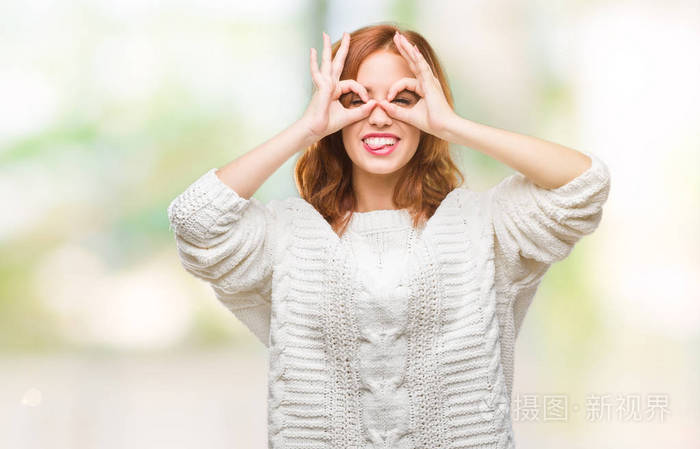 年轻漂亮的女人在孤立的背景上穿着冬天的毛衣，做着好的手势，就像望远镜伸出舌头，透过手指看眼睛。 疯狂的表情。