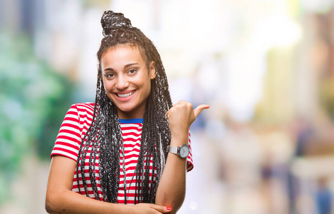 年轻的辫子非裔美国女孩在孤立的背景上微笑，快乐的脸，看着和指向一边，拇指向上。