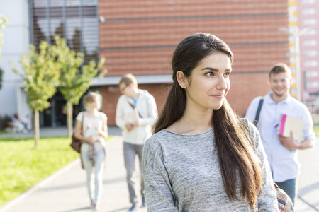 带着微笑的少女在大学校园里和朋友散步时向外张望