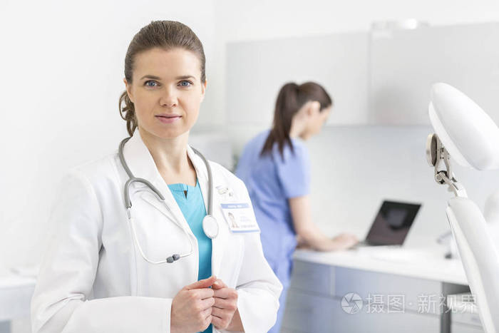 微笑的医生在诊所用笔记本电脑站在护士面前的画像