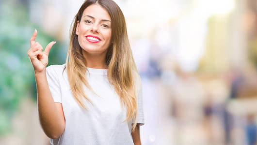 年轻漂亮的女人休闲白色T恤在孤立的背景上微笑和自信的手势与手做大小标志与手指，同时看和相机。 测量概念。
