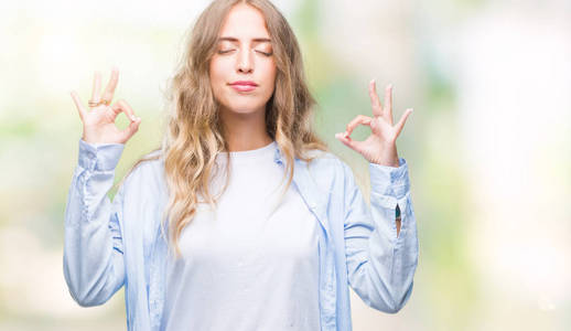 美丽的年轻金发女子在孤立的背景下放松和微笑，闭着眼睛做冥想手势与手指。 瑜伽概念。