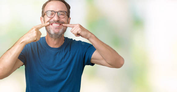 英俊的中年老人戴着眼镜，在孤立的背景上微笑，自信地展示和指着手指，牙齿和嘴。 健康概念。