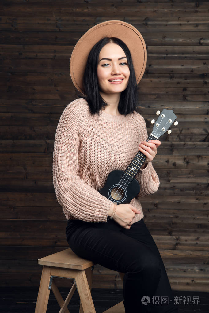 白人妇女在卷脖子毛衣和帽子唱歌激情和发挥四弦琴美丽的女歌手在室内