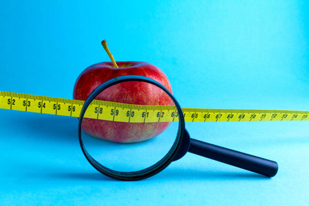 饮食观念。 减肥成功。 黄色的测量带和蓝色背景上的苹果。