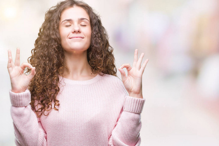 美丽的黑发卷发年轻女孩穿着粉红色的冬季毛衣，在孤立的背景下放松，微笑着闭着眼睛，用手指做冥想手势。 瑜伽概念。