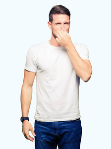 英俊的男人穿着休闲的白色T恤，闻着一些臭味和令人恶心的难以忍受的气味，用手指在鼻子上屏住呼吸。 难闻的概念。