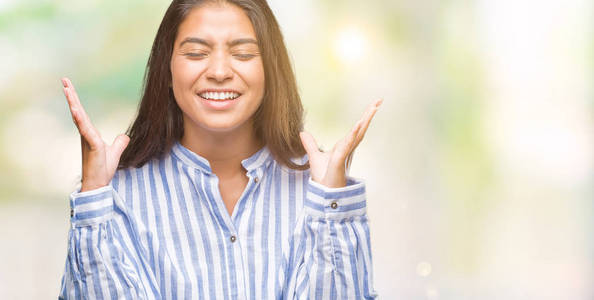 年轻美丽的阿拉伯女人在孤立的背景上庆祝疯狂和疯狂的成功，举起手臂和闭上眼睛尖叫兴奋。赢家概念