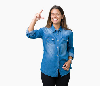 年轻漂亮的黑发女人穿着蓝色牛仔衬衫，在孤立的背景上微笑和自信的手势，用手指做尺寸标志，同时看和相机。衡量概念。