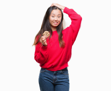 年轻的亚洲女人在孤立的背景下吃巧克力饼干，用手压在头上，羞愧和惊讶的脸震惊，愤怒和沮丧。因为错误而恐惧和不安。