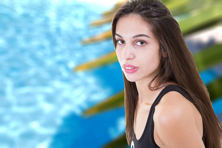 美丽的年轻黑发女孩在游泳池前蓝色撕裂的水与新鲜的绿色棕榈树叶。