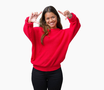 年轻美丽的深黑肤色的女人，穿着红色的冬毛衣，在孤立的背景下微笑，用手手掌和手指相机透视框架