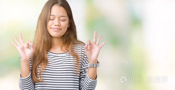 年轻漂亮的黑发女人穿着条纹毛衣，在孤立的背景上放松和微笑，闭着眼睛，用手指做冥想手势。 瑜伽概念。