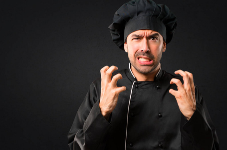 穿着黑色制服的厨师生气地做着愤怒的手势。 黑色背景下的负表达