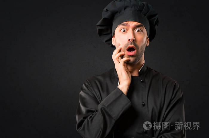 穿着黑色制服的厨师惊讶和震惊,同时向右看. 黑色背景下的面部表情