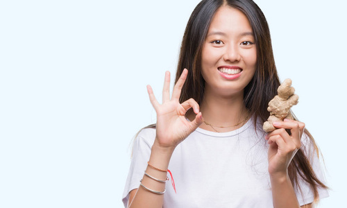 年轻的亚洲女人拿着新鲜的有机食品在孤立的背景上做OK标志，手指很好的象征