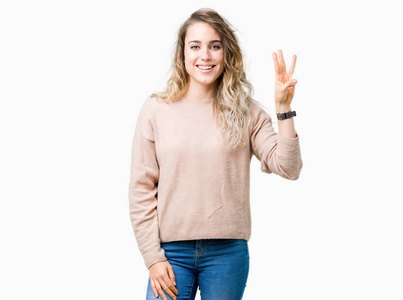 美丽的年轻金发女人穿着毛衣，穿着汗衫，在孤立的背景上展示和举着手指第三，同时微笑自信和快乐。